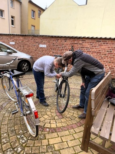 Ein Jugendlicher repariert unter Anleitung eines Erwachsenen ein Fahrrad auf dem Hof im Rahmen der mobilen Fahrradwerkstatt.