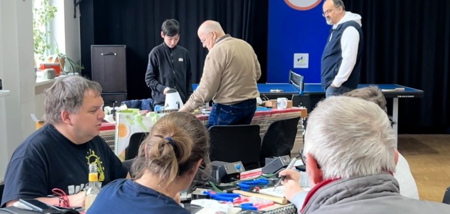 Mehrere Personen sitzen und arbeiten gemeinsam an verschiedenen Reparaturprojekten im Repair Café des JUKZ.