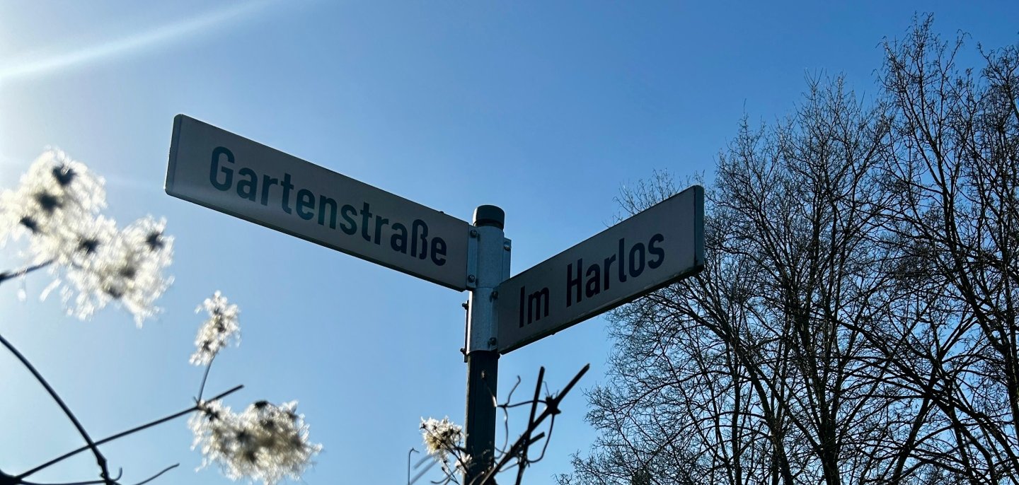 Zwei sich kreuzende Straßenschilder mit dem Name "Im Harlos" und "Gartenstraße"