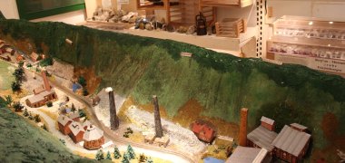 Ausstellung im Bergbaumuseum mit Modelllandschaft eines Industriegebiets, Gesteinsproben und historischen Dokumenten in Vitrinen.