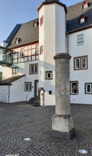 Historische Grenzsäule aus Lahnmarmor vor einem Fachwerkgebäude in Lahnstein, dem Nassau-Sporkenburger Hof, auf einem gepflasterten Platz.