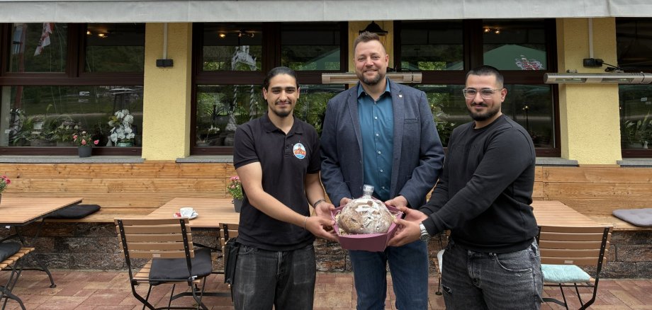 Neueröffnung von Alo's Rheinterrasse Gruppenfoto vor dem neu eröffneten Restaurant „Alo‘s Rheinterrasse“ in Niederlahnstein. Zu sehen sind die beiden Betreiber Robin und Rodi Hussein gemeinsam mit Oberbürgermeister Lennart Siefert. Im Hintergrund sind die Außenterrasse des Restaurants sowie der Rhein zu erkennen.