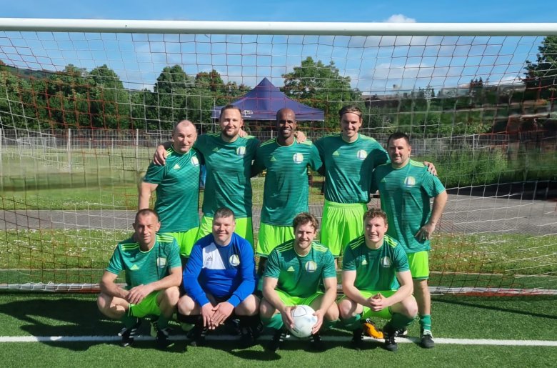 Benefiz-Fußballturnier für den guten Zweck in Lahnstein Ein Fußballteam in grünen Trikots und hellgrünen Shorts posiert für ein Foto vor einem Fußballtor auf einem Kunstrasenplatz. Vier Spieler stehen in der hinteren Reihe, fünf Spieler knien in der vorderen Reihe, wobei einer von ihnen einen Fußball vor sich hält.