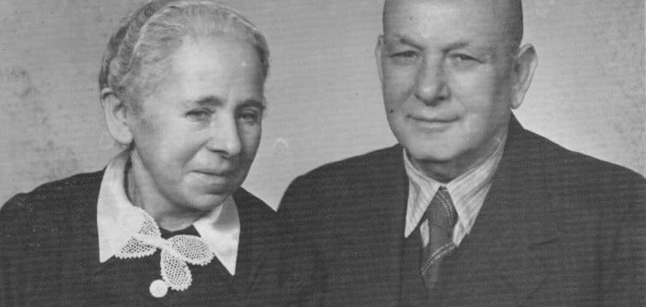 Emil und Johanna Baer Schwarz-Weiß-Porträt einer älteren Frau und eines älteren Mannes, die dicht nebeneinander vor einem einfarbigen Hintergrund stehen. Die Frau trägt ein dunkles Oberteil mit weißem Kragen und einer hellen Schleife. Der Mann trägt einen dunklen Anzug mit Hemd und Krawatte. Beide blicken in Richtung Kamera.