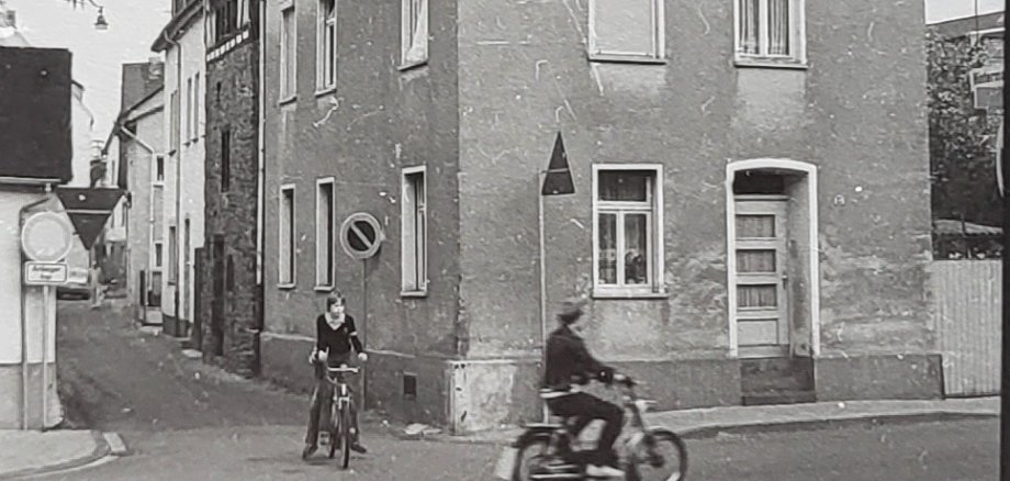Historische Schwarz-Weiß-Aufnahme einer Straßenecke in Lahnstein. Im Vordergrund fährt ein Mann auf einem Motorrad über die Straße, daneben steht ein Junge mit einem Fahrrad. Hinter einem mehrgeschossigen Wohnhaus erhebt sich ein massiver steinerner Turm. Links führt eine schmale Gasse zwischen den Häusern entlang.