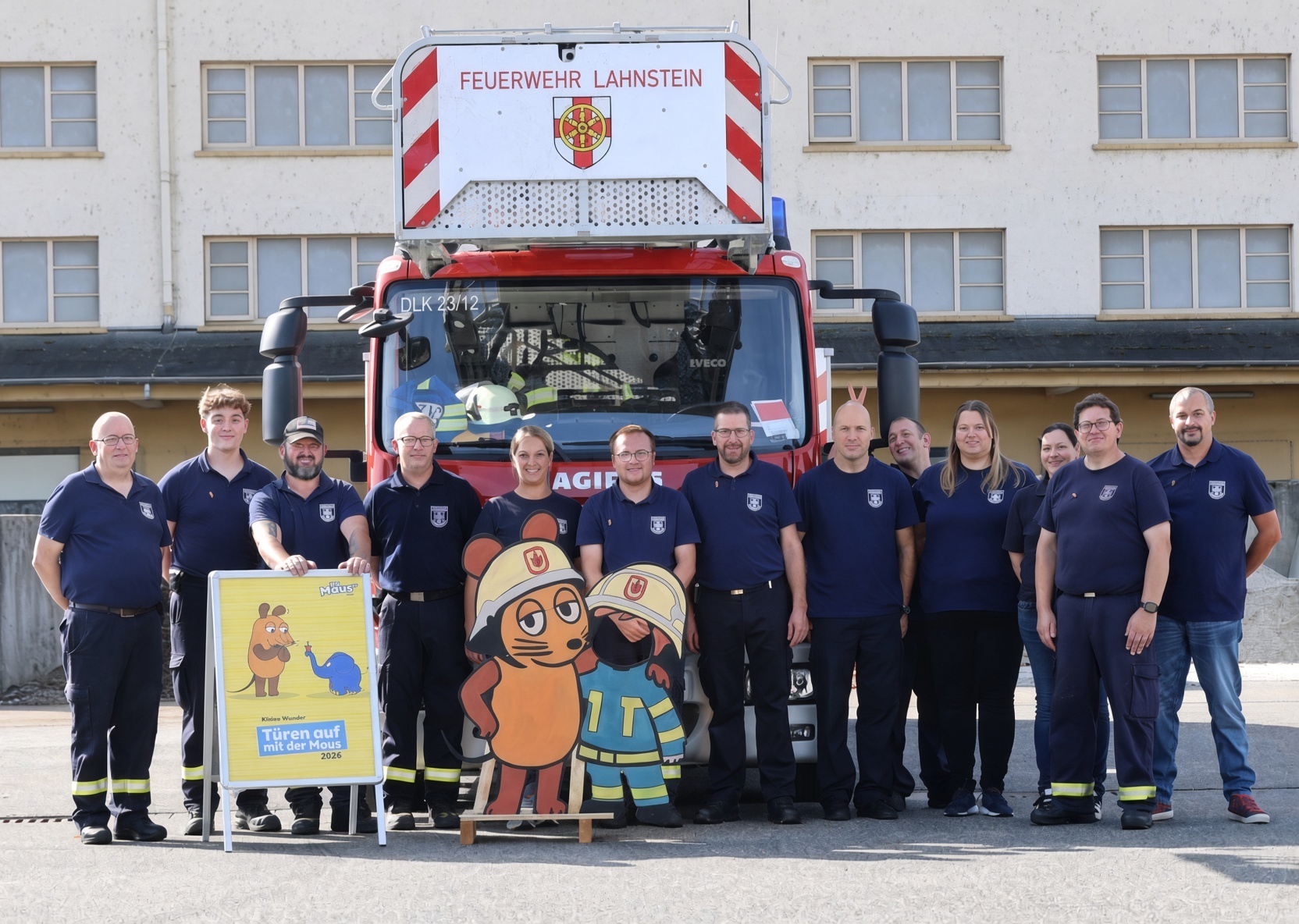 Gruppenfoto von Mitgliedern der Feuerwehr Lahnstein vor einem roten Feuerwehrfahrzeug mit Drehleiter. Vor der Gruppe stehen ein Aufsteller zur Aktion „Türen auf mit der Maus 2026“ sowie zwei große Figuren der Maus in Feuerwehrkleidung.