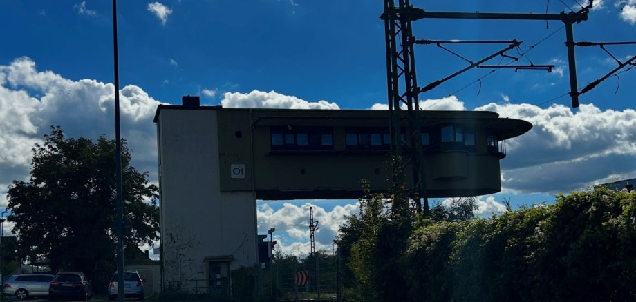 Bürgermeister-Müller-Straße Lahnstein Blick auf das Stellwerk an der Bürgermeister-Müller-Straße in Lahnstein. Im Vordergrund verläuft die Straße mit angrenzendem Gehweg. Rechts ragen ein Oberleitungsmast und Stromleitungen der Bahn in den Himmel. Im Hintergrund ist das Stellwerksgebäude mit seinem auskragenden oberen Geschoss zu sehen.