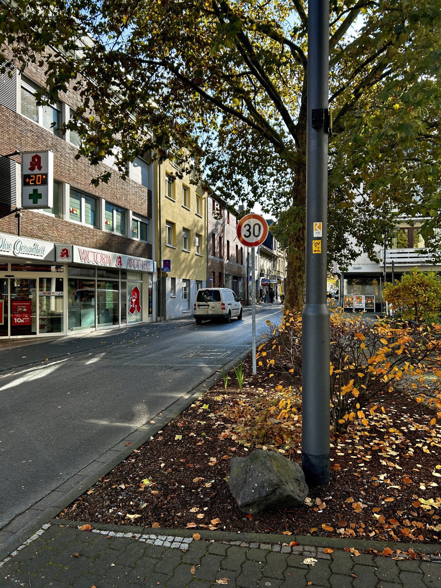 Blick auf die Adolfstraße in Lahnstein mit einem Tempo-30-Schild am Straßenrand. Links sind die Victoria-Apotheke und weitere Wohn- und Geschäftshäuser zu sehen. Rechts säumen große Bäume und herbstlich bepflanzte Grünflächen die Straße.