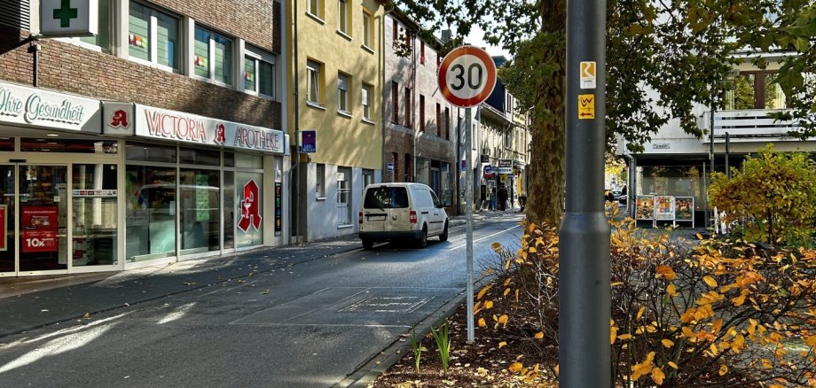 Adolfstraße Lahnstein Blick auf die Adolfstraße in Lahnstein mit einem Tempo-30-Schild am Straßenrand. Links sind die Victoria-Apotheke und weitere Wohn- und Geschäftshäuser zu sehen. Rechts säumen große Bäume und herbstlich bepflanzte Grünflächen die Straße.