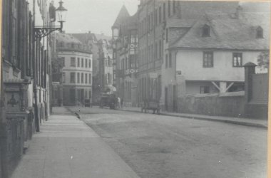 Erkennen Sie Lahnstein? Historische Schwarz-Weiß-Aufnahme der Lahnsteiner Hochstraße. Entlang der Straße stehen dicht aneinandergebaute Häuser, darunter Fachwerkgebäude. In der Ferne sind ein Pferdefuhrwerk und einige Personen zu erkennen.