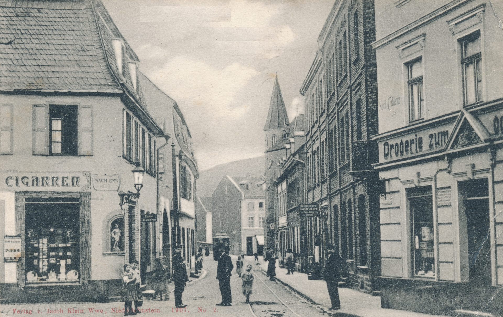 Historische Aufnahme der Hochstraße aus dem Jahr 1907. Zu sehen sind zahlreiche Wohn- und Geschäftshäuser mit damaligen Ladenbeschriftungen. Mehrere Erwachsene und Kinder stehen auf der Straße; im Hintergrund erhebt sich ein Kirchturm.