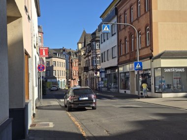 Erkennen Sie Lahnstein? Heutiger Blick in die Hochstraße bei sonnigem Wetter. Die Straße wird von Wohn- und Geschäftshäusern gesäumt, am Straßenrand stehen Autos. Im Hintergrund sind historische Gebäude und ein Turm zu sehen.