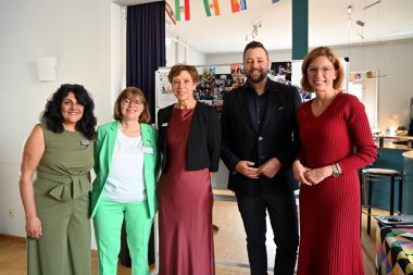 Nasstaran Houshmand vom JUKZ, Oberbürgermeister Lennart Siefert und Ministerin Sabine Bätzing-Lichtenthäler Fünf Personen, vier Frauen und ein Mann, stehen nebeneinander in einem Veranstaltungsraum des Jugendkulturzentrums und schauen in die Kamera. Im Hintergrund sind eine Fotowand sowie mehrere kleine Flaggen zu sehen.