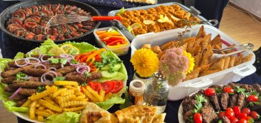 Internationales Buffet Mehrere mit dunkelblauen Tüchern bedeckte Tische sind mit zahlreichen Speisen gefüllt. Zu sehen sind unter anderem verschiedene gefüllte und gebackene Teigwaren, Fleischgerichte, Salate, Gemüse, Gebäck und weitere Speisen auf Platten, Tellern und in Schalen. Zwischen den Gerichten stehen kleine Blumenvasen.