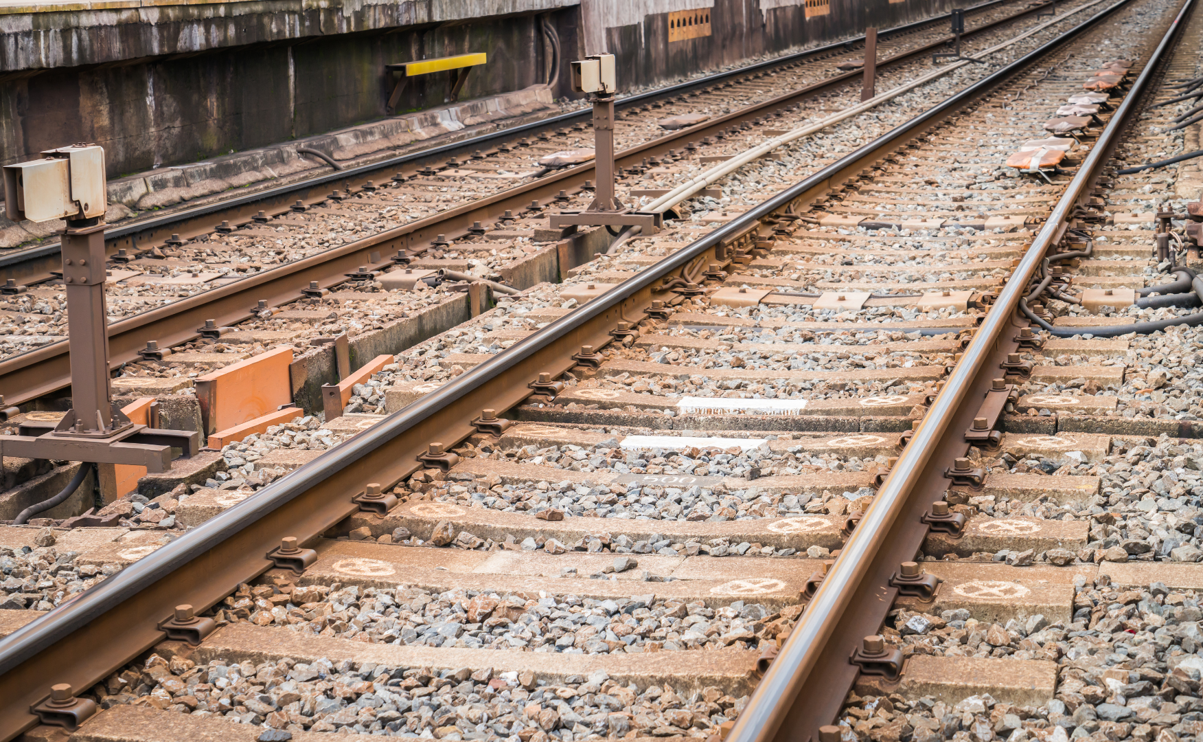 Mehrere parallel verlaufende Bahngleise mit Schotterbett und Betonschwellen sind aus der Nähe zu sehen. Im Gleisbereich befinden sich Weichen, Kabel und technische Anlagen der Bahninfrastruktur. Die Schienen verlaufen diagonal durch das Bild und vermitteln den Eindruck eines weitläufigen Gleisfeldes.