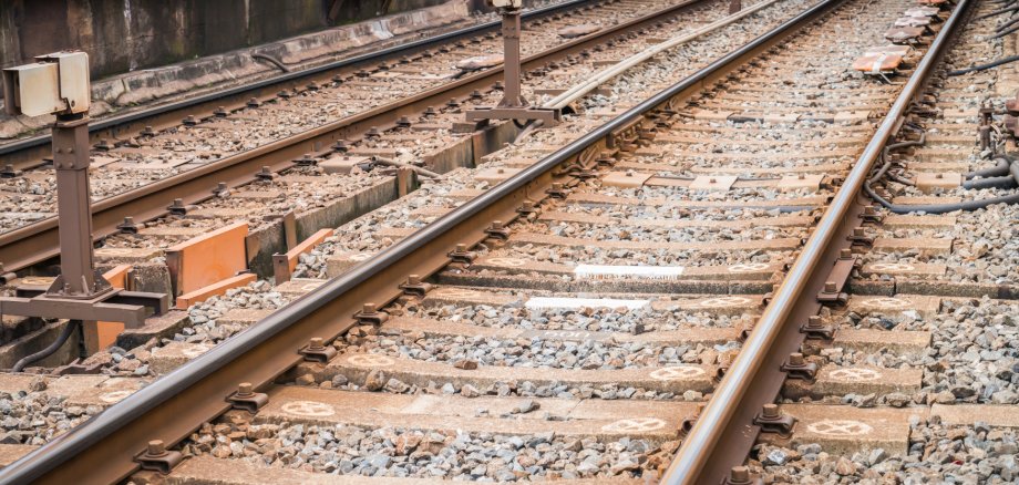 Mehrere parallel verlaufende Bahngleise mit Schotterbett und Betonschwellen sind aus der Nähe zu sehen. Im Gleisbereich befinden sich Weichen, Kabel und technische Anlagen der Bahninfrastruktur. Die Schienen verlaufen diagonal durch das Bild und vermitteln den Eindruck eines weitläufigen Gleisfeldes.