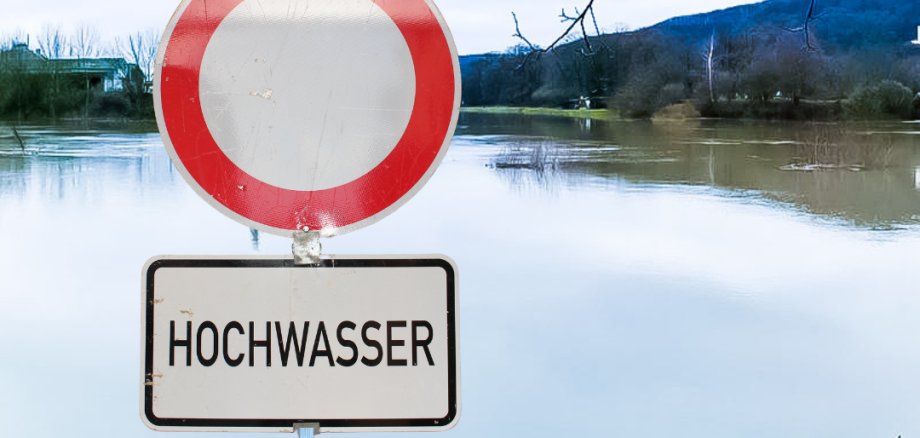 Ein "Durchfahrt-verboten-Schild" mit dem Zusatzwarnhinweis "Hochwasser", das unmittelbar vor einem überschwemmten Bereich steht.