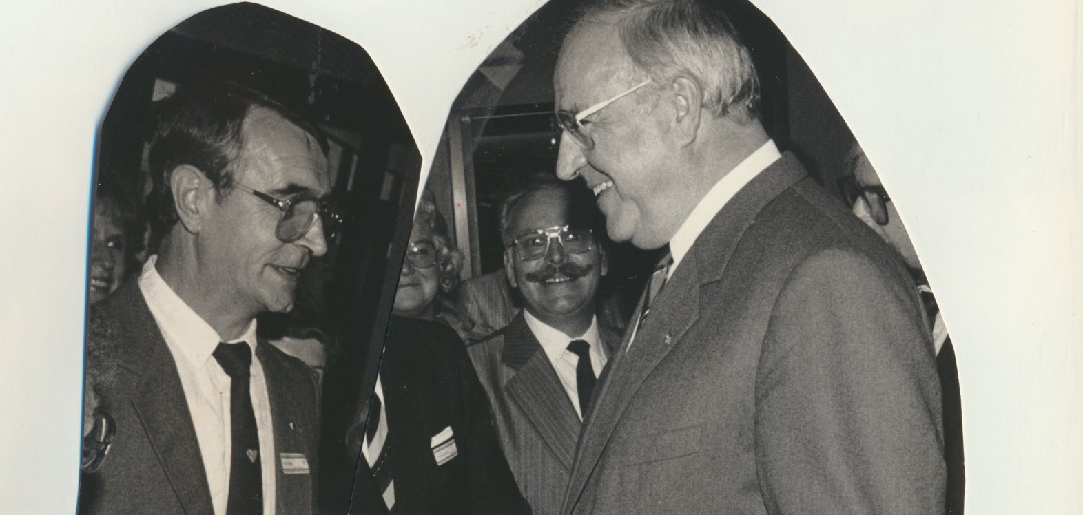 Schwarz-Weiß-Foto: Zwei Männer in Anzügen, rechts steht der damalige Bundeskanzler Helmut Kohl, links der gewürdigte Hans Hoffmann aus Lahnstein, stehen einander bei einer Veranstaltung gegenüber und unterhalten sich. Im Hintergrund sind weitere lächelnde Personen zu sehen.