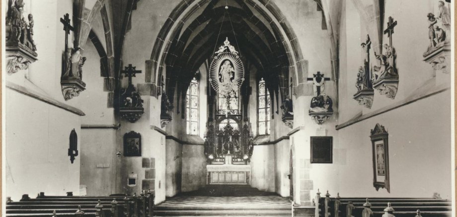 Allerheiligenbergkapelle Lahnstein Historische Schwarz-Weiß-Aufnahme des Innenraums der Allerheiligenbergkapelle in Lahnstein. Der Blick führt zwischen den hölzernen Kirchenbänken zum reich verzierten Altar mit einer Marienfigur. Spitzbogengewölbe, hohe Kirchenfenster und Kreuzwegstationen an den Seitenwänden prägen den Kirchenraum.