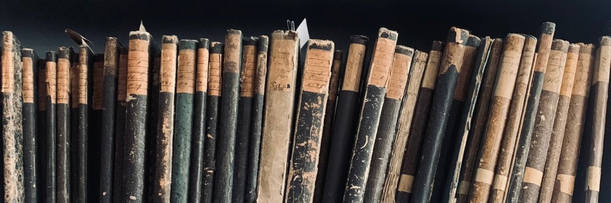 Stadtarchiv Lahnstein Drei Regalböden mit zahlreichen alten Büchern unterschiedlicher Größe. Die Einbände sind stark gealtert, teilweise beschädigt oder verblasst. Viele Buchrücken tragen handschriftliche oder gedruckte Rückenschilder. Die Bücher stehen dicht nebeneinander und zeigen deutliche Gebrauchsspuren.