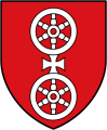 Rotes Wappen mit zwei silbernen, übereinander angeordneten sechsspeichigen Rädern. Zwischen den Rädern befindet sich ein silbernes Kreuz.