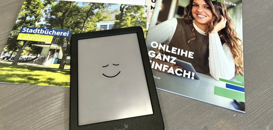 eBook-Sprechstunde in der Stadtbücherei Auf einem Tisch in der Stadtbücherei Lahnstein liegen ein Tolino-eReader, Informationsbroschüren zur Onleihe und eine Kurzanleitung. Im Hintergrund sind mehrere Bücherregale mit Romanen und Sachbüchern zu sehen.