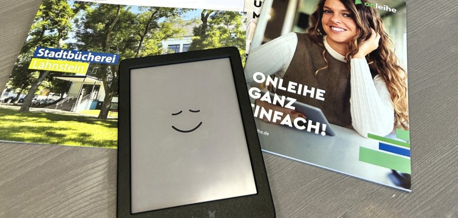 eBook-Sprechstunde in der Stadtbücherei Auf einem Tisch in der Stadtbücherei Lahnstein liegen ein Tolino-eReader, Informationsbroschüren zur Onleihe und eine Kurzanleitung. Im Hintergrund sind mehrere Bücherregale mit Romanen und Sachbüchern zu sehen.