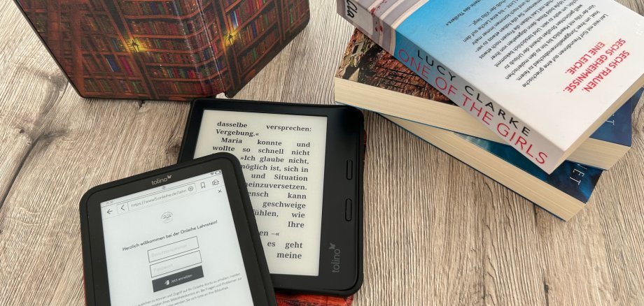 eBook-Sprechstunde in der Stadtbücherei Lahnstein Auf einem Tisch befinden sich zwei ebook-Reader, im Hintergrund ein aufstellter eBook-Reader mit einer Hülle, die viele Bücherreihen zeigt, sowie ein Stapel von mehreren Büchern