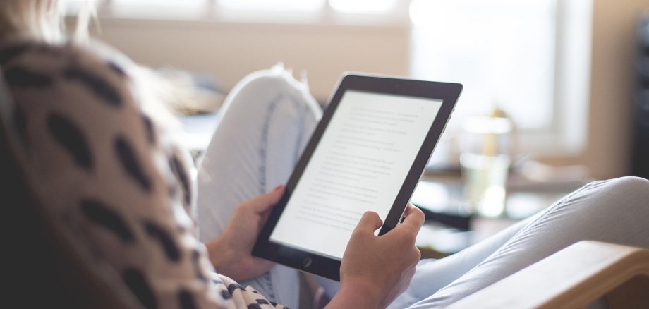 Eine Frau sitzt auf einem Stuhl und liest ein eBook.