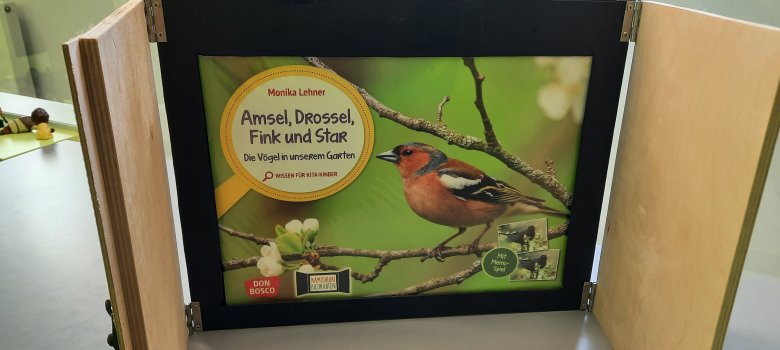 Kamishibai-Erzähltheater in der Stadtbücherei Lahnstein Aufgeklapptet Kamishibai-Erzähltheater mit einem Vogel und Geäst vor grünem Hintergrund, thematisch zu Natur mit Aufschrift "Amsel, Drossel, Fink und Star