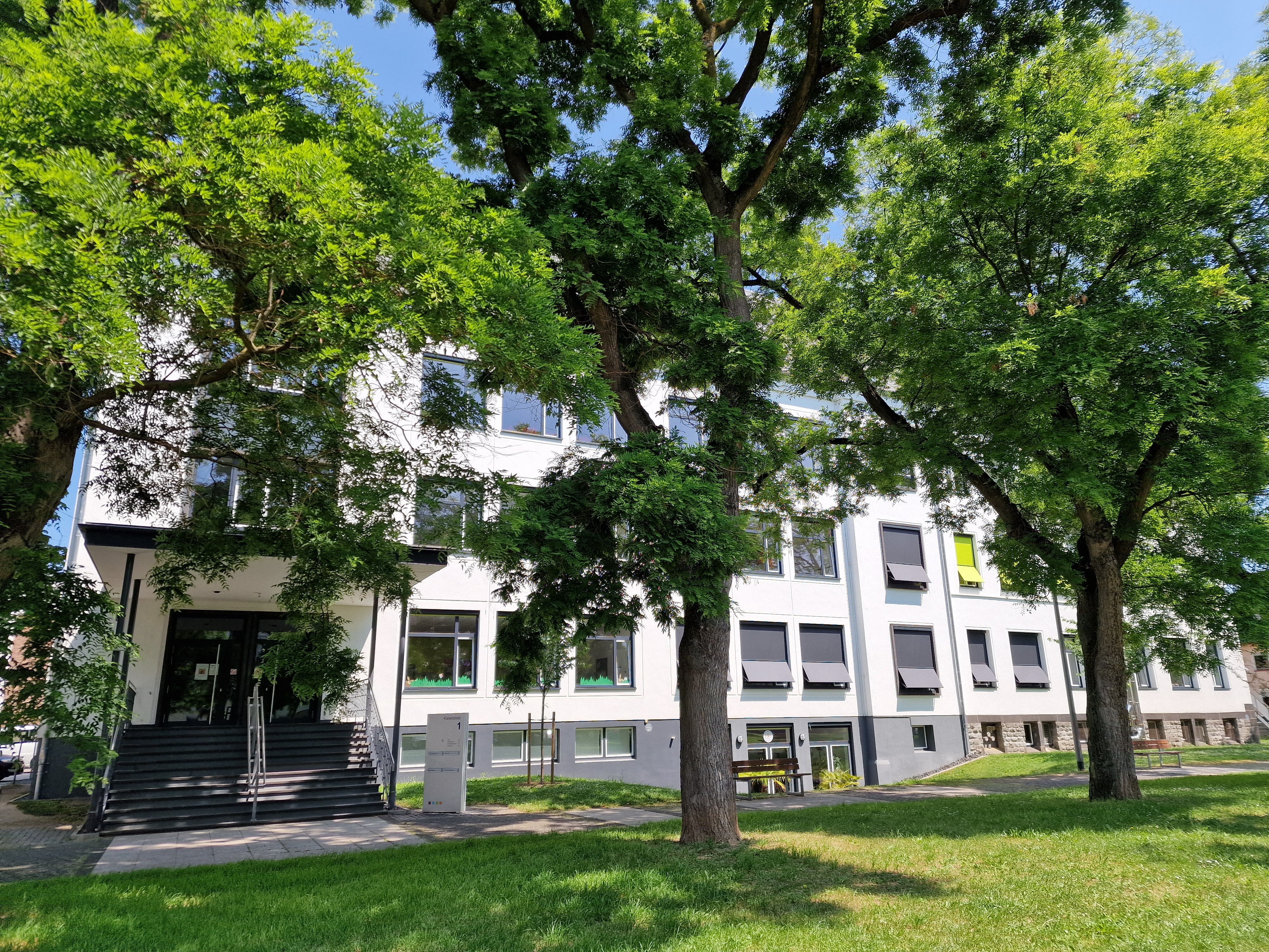 Außenansicht der Stadtbücherei Lahnstein am Kaiserplatz mit Eingangsbereich mit grüner Wiese und Bäumen