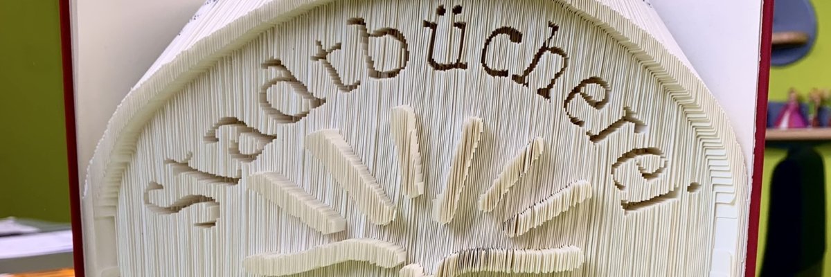 Künstlerisch gefaltetes Buch, dessen Seiten den Schriftzug „Stadtbücherei Lahnstein – vielfältig und informativ“ darstellen.