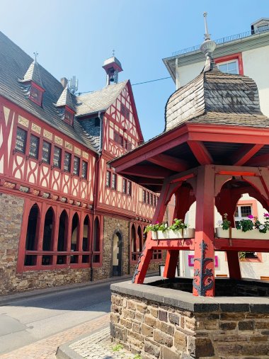 Altes Rathaus Lahnstein mit Marktbrunnen Historisches Fachwerkgebäude mit roter Fassade und einem roten Brunnen oder Pavillon im Vordergrund. Mehrere Fenster und Fachwerkelemente prägen das Bild.