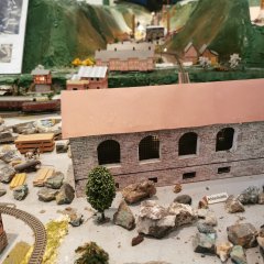 Modell des Bergmannsdorf um 1900 im Bergbaumuseum Friedrichssegen Modell eines länglichen Industrie- oder Wirtschaftsgebäudes mit hellem Mauerwerk und rotem Dach. Das Gebäude besitzt mehrere Rundbogenfenster und ist von kleinen Modelllandschaften umgeben. Das Modell stellt das Bergbaudorf Friedrichssegen um das Jahr 1900 dar.