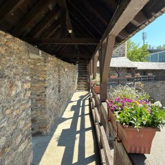 Hexenturm Lahnstein Wehrgang Überdachter Wehrgang entlang einer Steinmauer. Im Hintergrund stehen blühende Pflanzen in einem Innenhof.