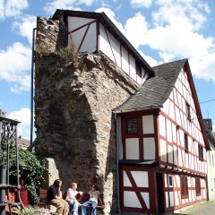 Stadtmauerhäuschen Lahnstein Außenansicht eines historischen Fachwerkhäuschens unter blauem Himmel, das direkt an die Stadtmauer Stadtmauer angebaut ist. Auf einer Bank sitzen zwei Mädchen.