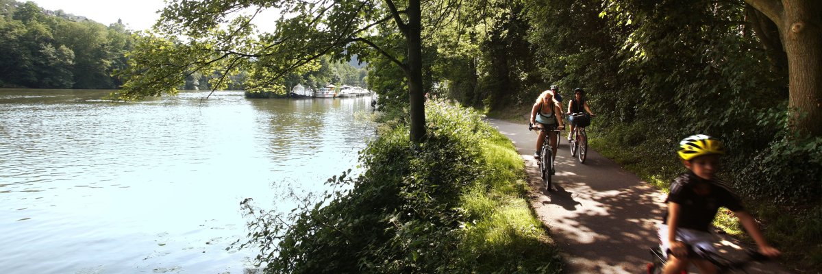Drei Radfahrer auf einem befestigten Weg entlang des Lahnzfers.