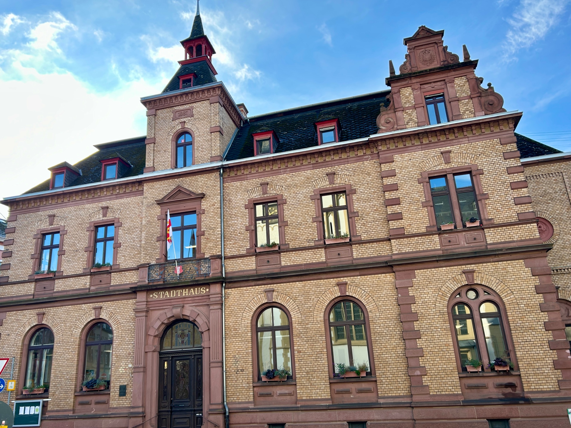 Historisches Stadthaus in Lahnstein mit repräsentativer Fassade aus gelbem Backstein und rötlichem Sandstein. Über dem Haupteingang steht der Schriftzug „Stadthaus“. Das Gebäude besitzt Rundbogenfenster, verzierte Giebel und einen markanten Turm mit spitzem Dach.